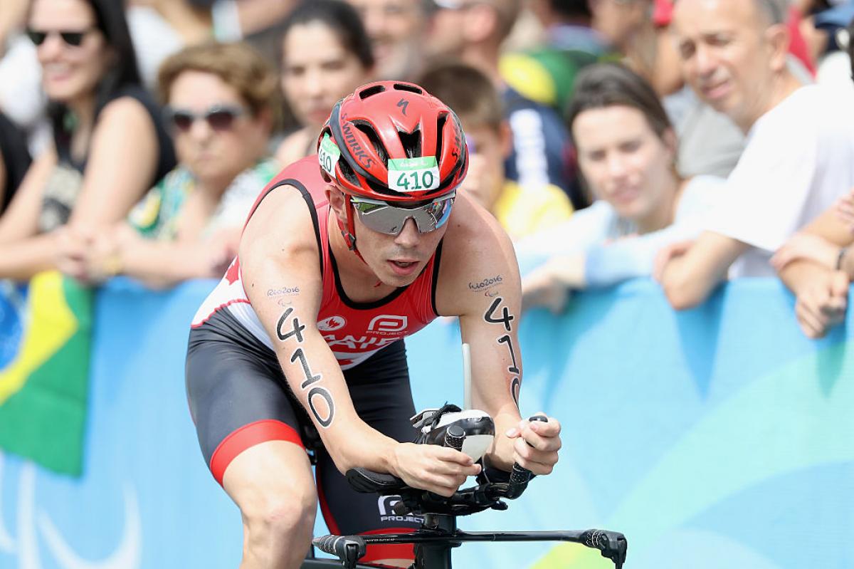 Stefan Daniel in a red Canada kit leans forward on his bike in front of a crowd at Rio 2016